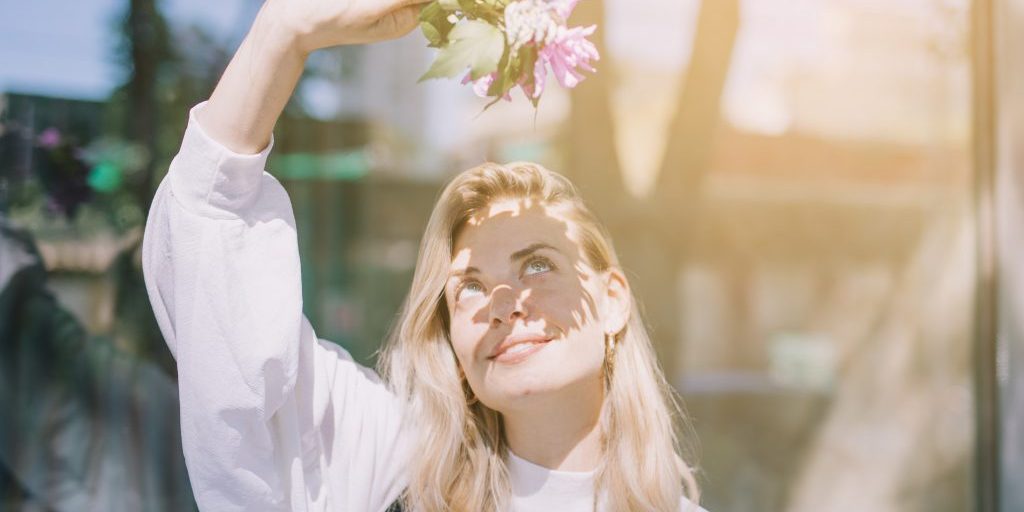 blonde-young-woman-holding-flowers-hand-shielding-her-eyes-from-sunlight