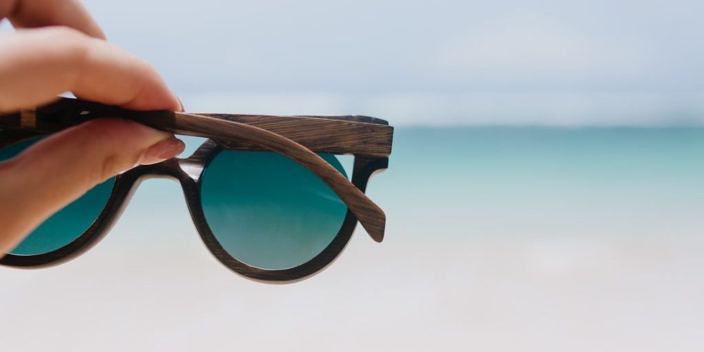 Outdoor photo of ocean with female hand on foreground. Woman holding summer sunglasses on sea background.