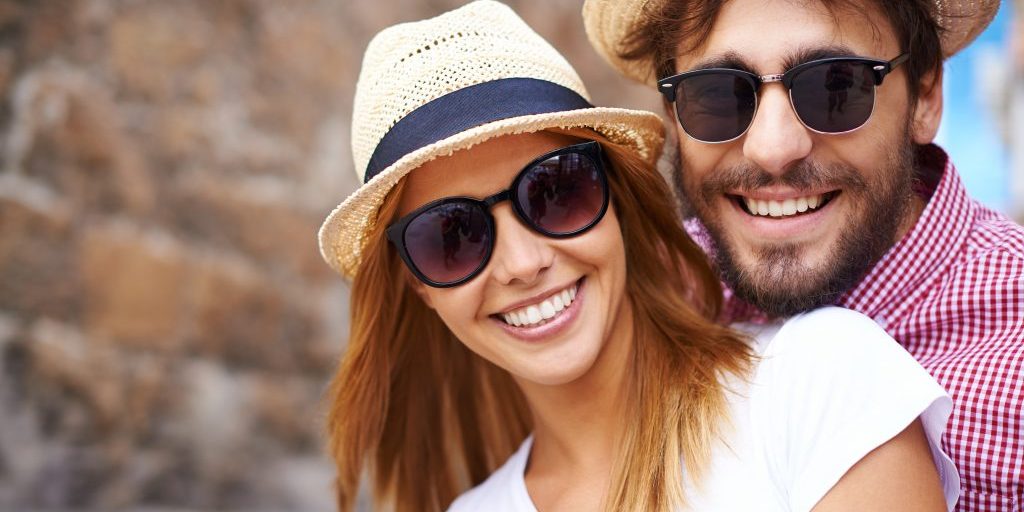 Happy girl and her boyfriend in hats and sunglasses looking at camera