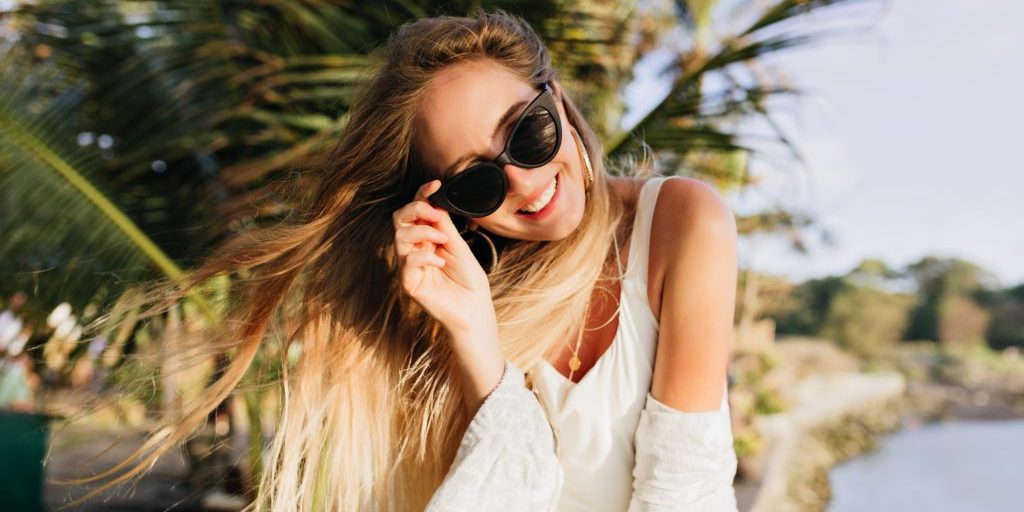 Portrait of pretty european girl with cute smile spending time at exotic beach. Outdoor photo of attractive female model posing with long hair waving at resort.
