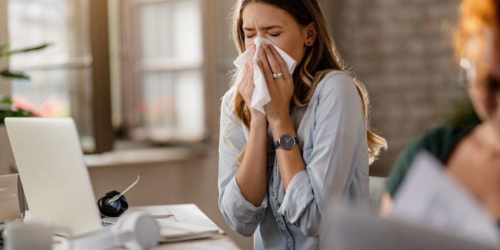 Young sick businesswoman sneezing in a tissue while working in the office.